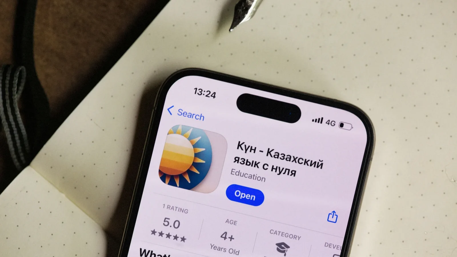 Close-up of a smartphone screen showing a Kazakh language learning app in an open notebook setting.