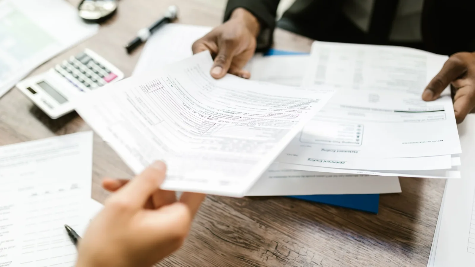 Two professionals exchanging documents in an office setting, focusing on paperwork and data analysis.