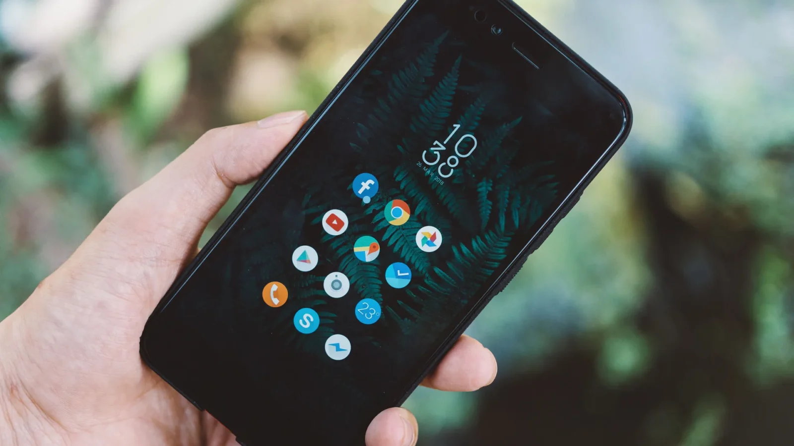 Close-up of a hand holding a smartphone with app icons and a nature wallpaper.