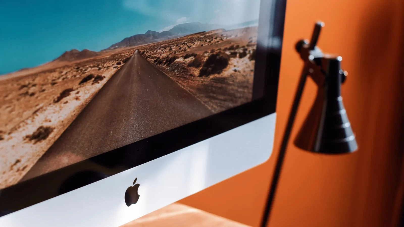 A sleek modern workspace featuring an iMac displaying a desert road and a stylish desk lamp.
